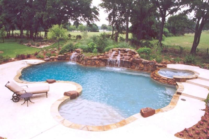 This Denton, Texas swimming pool incorporates a large boulder wall with two impressive waterfalls that are bordered by the elevated spa and diving board, a stained concrete deck, Oklahoma flagstone coping, large accent boulders starting at the tanning ledge and a lagoon pebble interior finish.