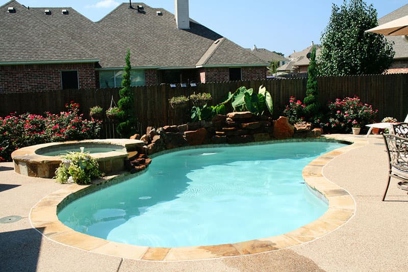 This Corinth, Texas swimming pool features Large boulder waterfalls, an elevated Oklahoma flagstone coping spa with boulder spillway, concrete spray-decking, Oklahoma flagstone coping and white plaster finish.