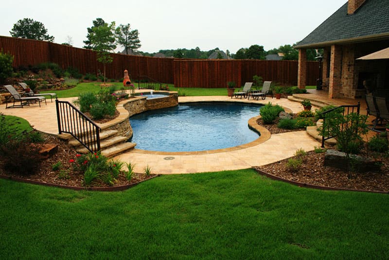 This Denton, Texas swimming pool is located in the Forrestridge neighborhood and features a multi-level stamped concrete deck, Oklahoma flagstone coping, a stacked stone raised beam, elevated spa with irregular stacked flagstone spillway, Oklahoma flagstone steps, landscaping planters and midnight blue aggregate finish interior.