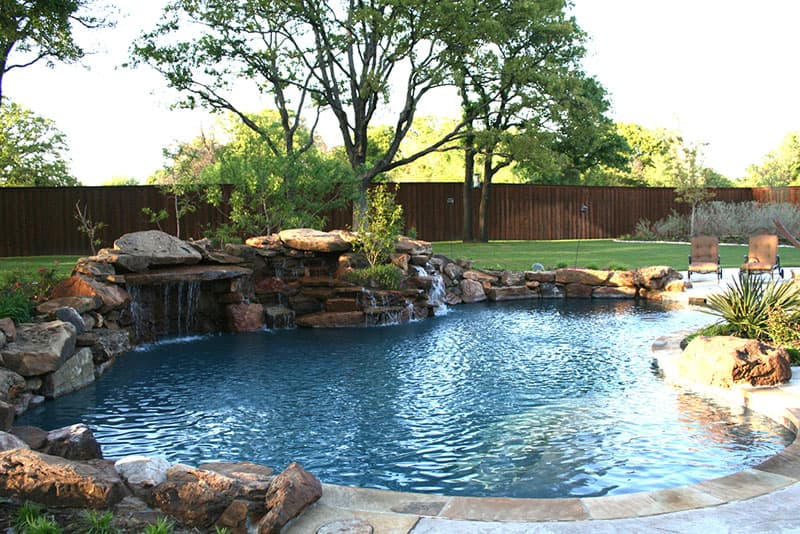 This Denton, Texas families dream pool features multiple massive boulder waterfalls with a large shelf stone grotto and planters set inside the boulders, stamped concrete decking, Oklahoma flagstone coping, a large tanning ledge and pebble finish interior.