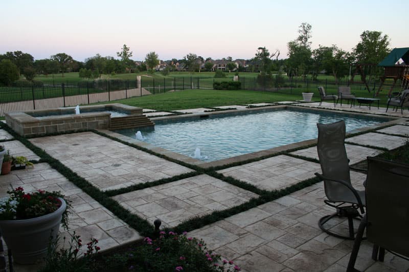 This Flower Mound pool/spa combination uses separations between the stamped concrete decking to define the architects concept. Water features accent the tanning ledge as the spillway directs water from the elevated spa onto it. This project is completed with the choice of Oklahoma coping and a dark blue pebble finish.