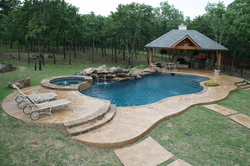 Carved into this Argyle, Texas hillside as if its soul beginning purpose was to end there sits this waterfall enriched residential swimming pool. The moss boulder waterfall extends from the elevated spa to the arbor enclosed outdoor kitchen. Stamped concrete decking lends access to the Oklahoma coping of the Midnight blue pebblesheen finish swimming pool.