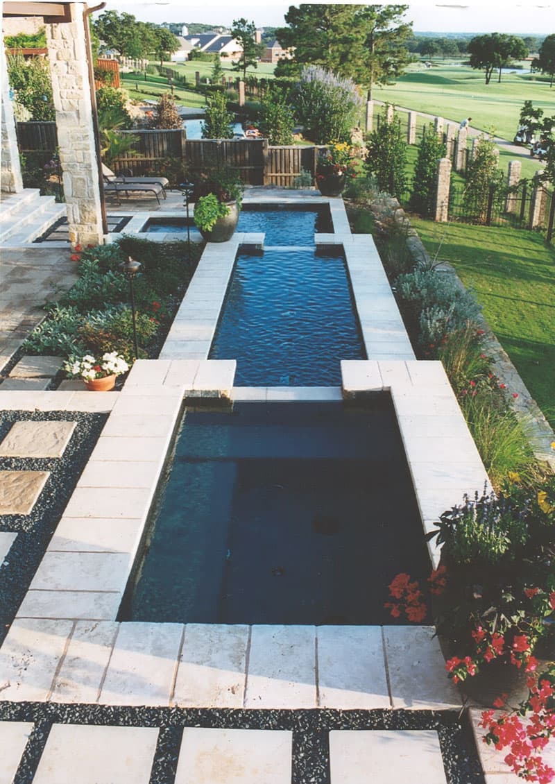 The tumbled travertine coping of this three tiered Spa – Fountain – Pool match the poured in place stamped concrete decking of this award-winning Corinth, Texas residential swimming pool.