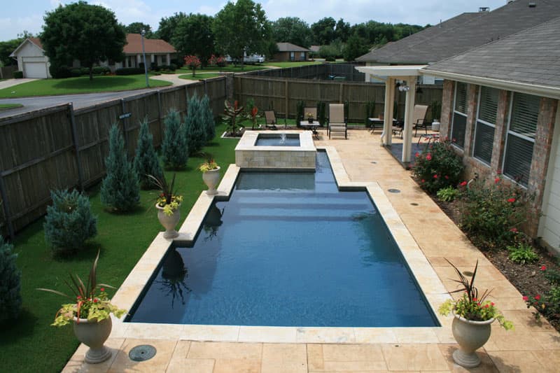 This Corinth, Texas swimming pool incorporates stamped decking and a honed travertine coping to accent the deep blue aggregate pool finish as the notched spillway of the elevated spa spills into the pool.