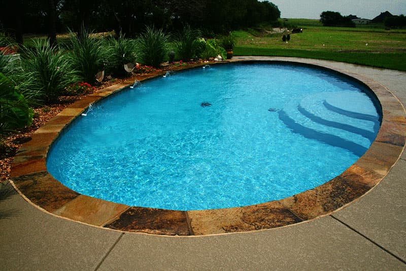 This Sanger, Texas area oval shaped swimming pool was designed for relaxation and water aerobics, with the Tahoe blue interior, Oklahoma coping and spray-deck concrete serving as material selections. The 4 aerators spray cool water over the pool to curve those midsummer water temperatures.