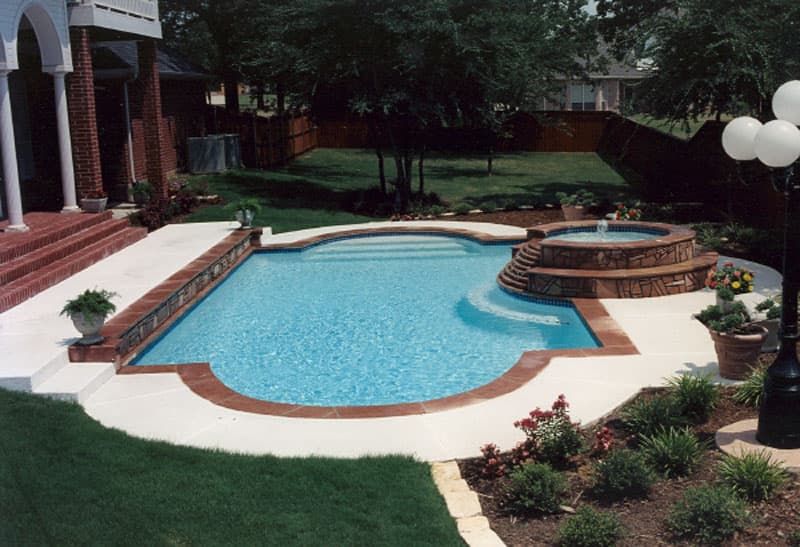 This Denton, Texas swimming pool has a formal look with the light colored spray-deck, Colorado flagstone coping, white plaster finish, stone veneered raised wall and multi-level raised spa.
