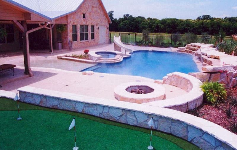 Aubrey, Texas is the home of this outdoor masterpiece. A pebblesheen beach entry leads you into the pristine blue water as you are surrounded by large slabs of white boulder waterfalls opposing an elevated spa with tiered spillway and a water slide. After your swim you can warm up by the matching stone firepit and relax on the custom putting green.