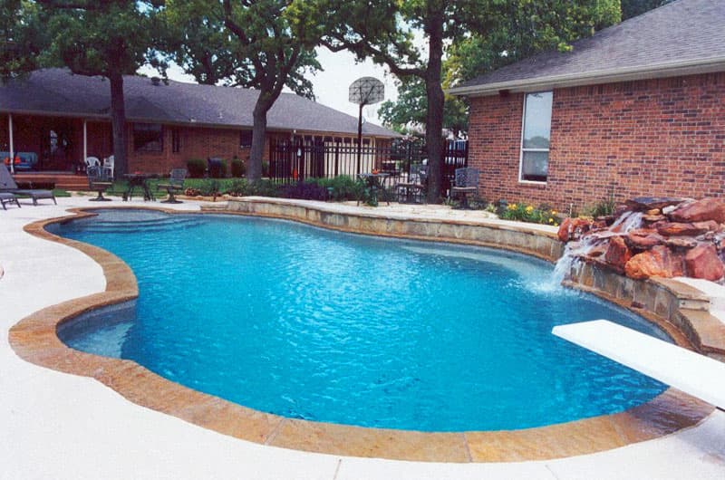 This Denton, Texas diving pool displays a unique use of Colorado flagstone coping, buff spray-decking, moss boulder waterfall with an irregular pattern veneered raised beam and white plaster to create this families dream pool.