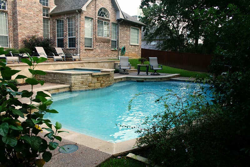 This Corinth, Texas swimming pool features ; an elevated washed aggregate deck, lueters coping, white plaster interior and a raised spa veneered in a 3 unit lueters stone.