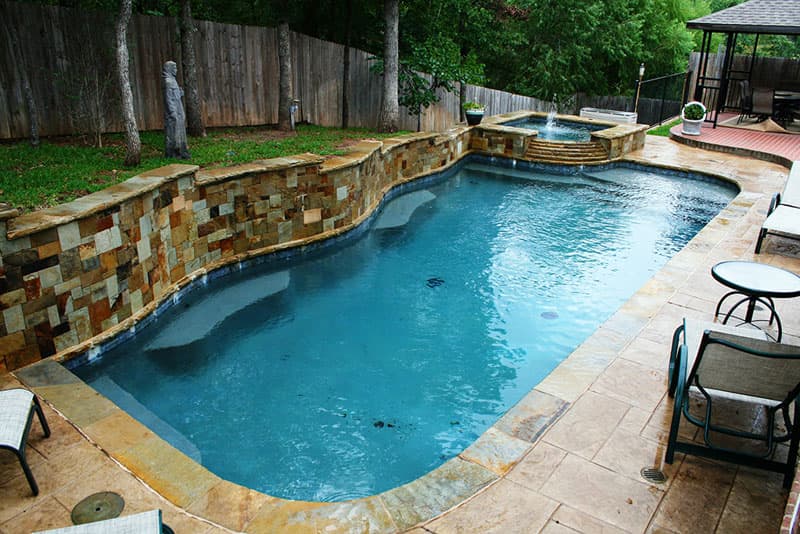 The hand cut Oklahoma veneer on the multi-level raised beam blend into the elevated spa as it spills into the Tahoe blue aggregate finish of this Corinth, Texas swimming pool. The Oklahoma flagstone coping and pattern stamped concrete decking complete the design.