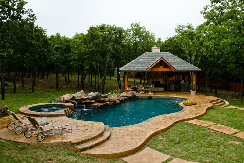 Carved into this Argyle, Texas hillside as if its soul purpose was to end there sits this waterfall enriched residential swimming pool. The moss boulder waterfall extends from the elevated spa to the arbor enclosed outdoor kitchen. Stamped concrete decking lends access to the Oklahoma coping of the Midnight blue pebblesheen finish swimming pool.
