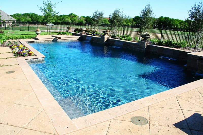 This Argyle, Texas swimming pool features travertine coping, stamped concrete multi-level decking, a raised beam with columns and an elevated spa with a stainless steel spillway.