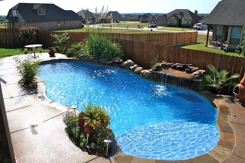 This Argyle, Texas swimming pool features a boulder waterfall with Oklahoma flagstone shelf rock spillway, Oklahoma coping, concrete spray-decking, a large tanning ledge and deck-jet water features that spray into the superblue aggregate interior finish.