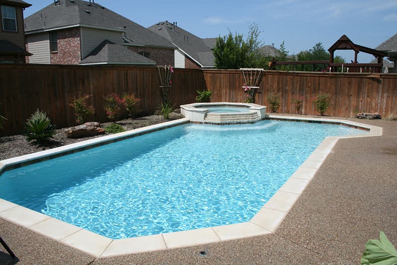 This Lantana, Texas swimming pool features white precast coping and a matching veneered elevated spa, white plaster finish and a washed aggregate decking.