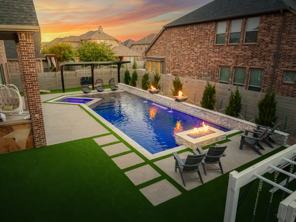 A picture of a pool with three fire pits in a manicured backyard.