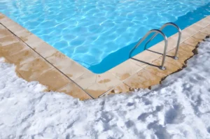 Corner of a pool in winter with snow around the edge.