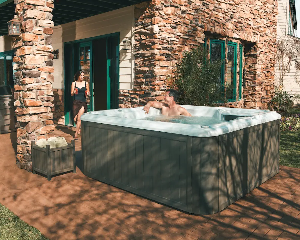 Picture of a wife bringing out cold drinks to her husband who is sitting in a hot tub.